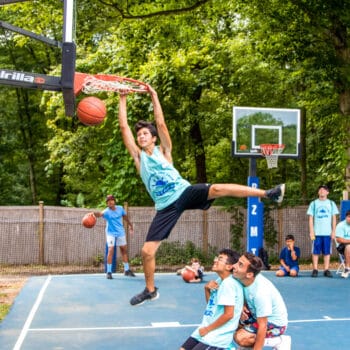 A camper dunking a basketball while his friends watch.