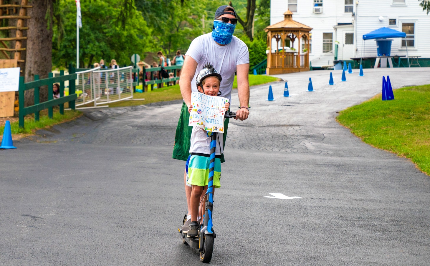 A camper on a scooter going down the camp driveway.