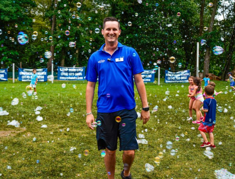 A camp staff member smiling while soap bubbles are floating in the air.