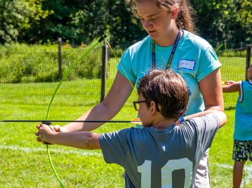 A camper learning how to shoot a bow and arrow.