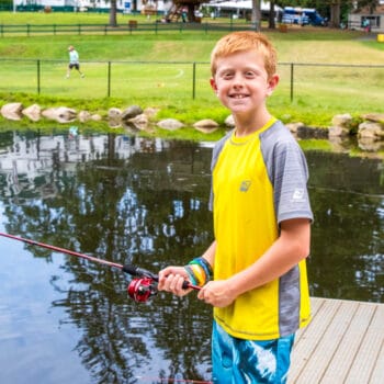A camper fishing and smiling on the dock.
