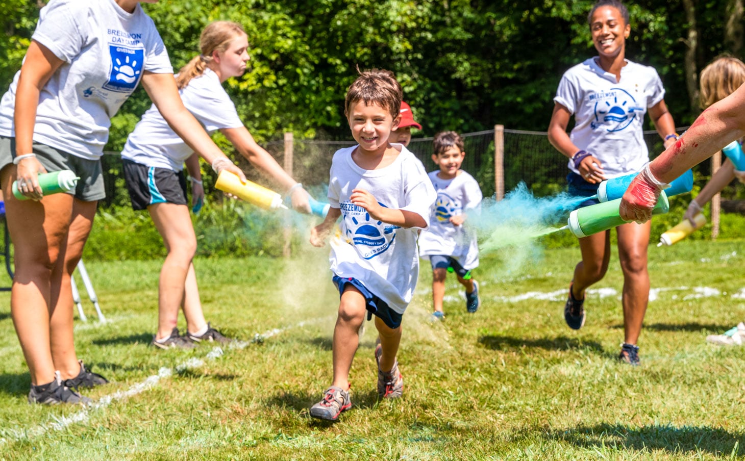 A camper running through colorful dust while smiling and laughing.